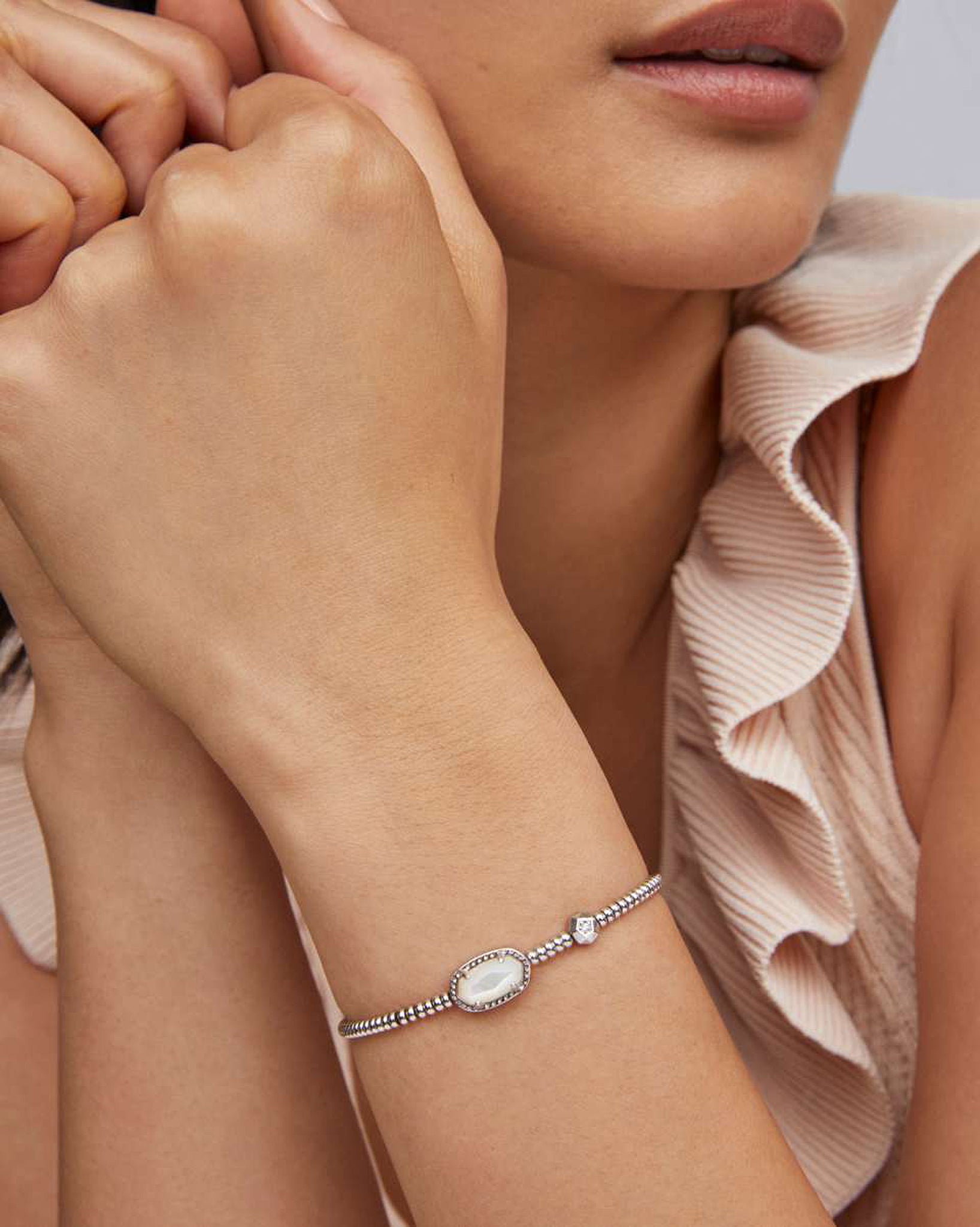 Close-up of a person wearing a bracelet with a white stone on a light background