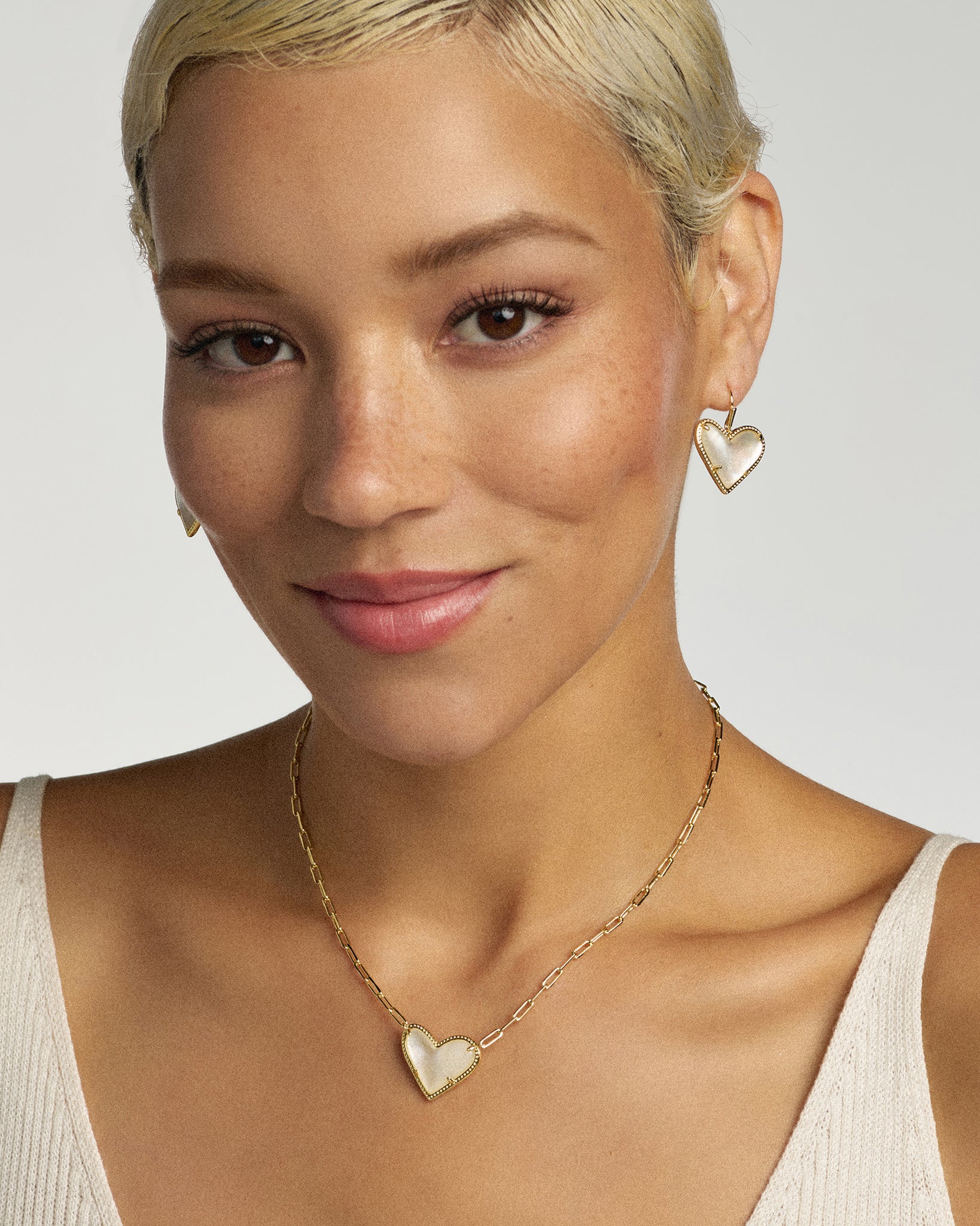 Woman wearing gold heart-shaped earrings and necklace on a plain background