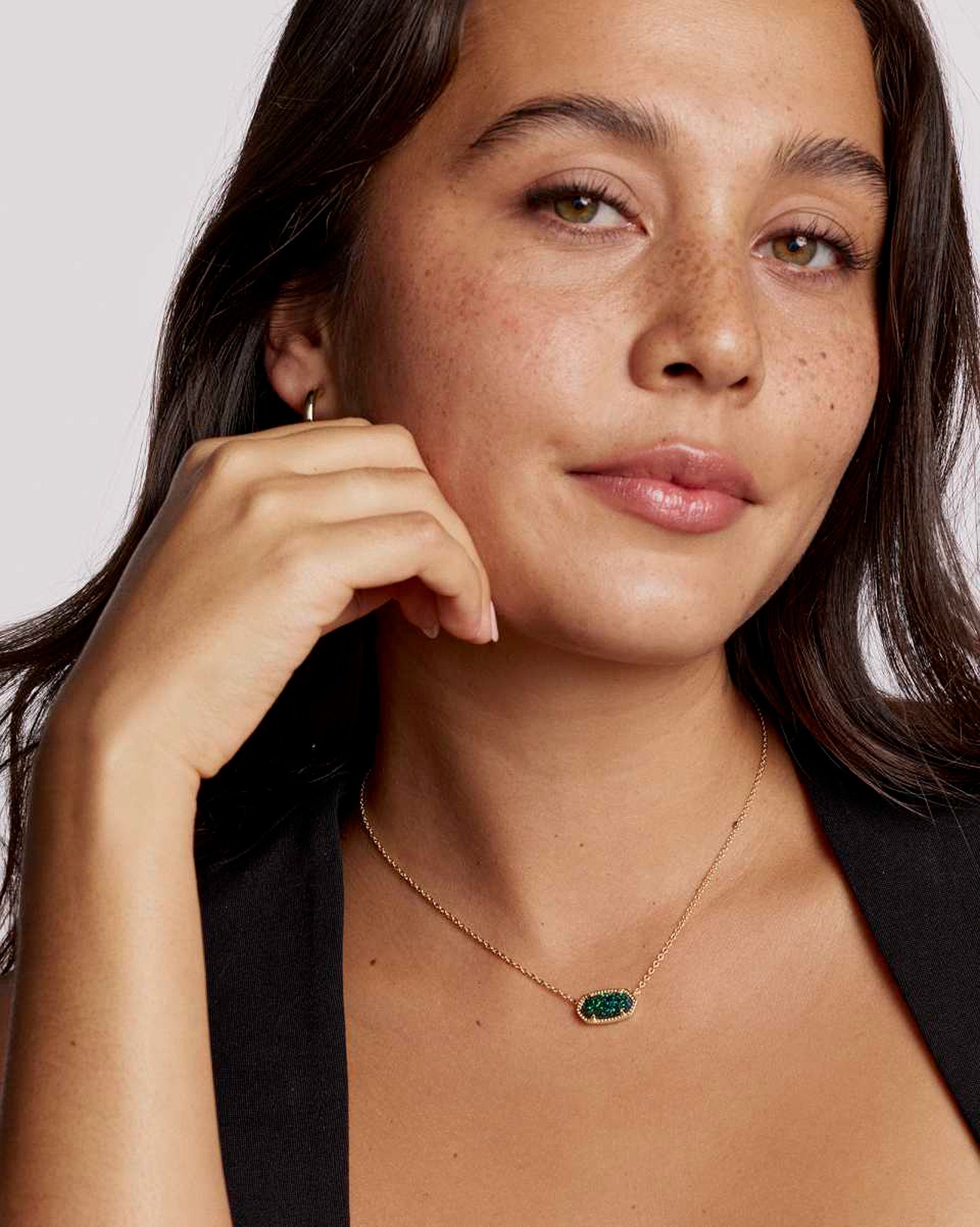 Woman wearing a gold necklace with an oval emerald pendant against a neutral background