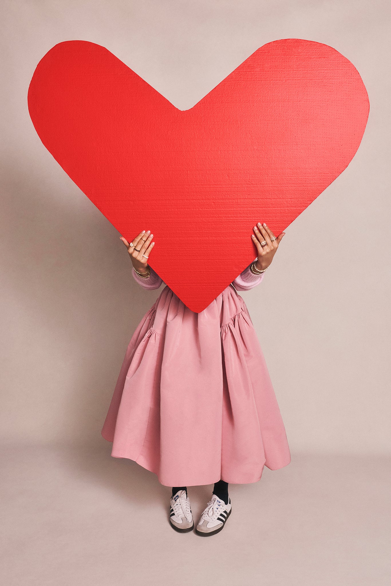 Person holding a large red heart against a beige background