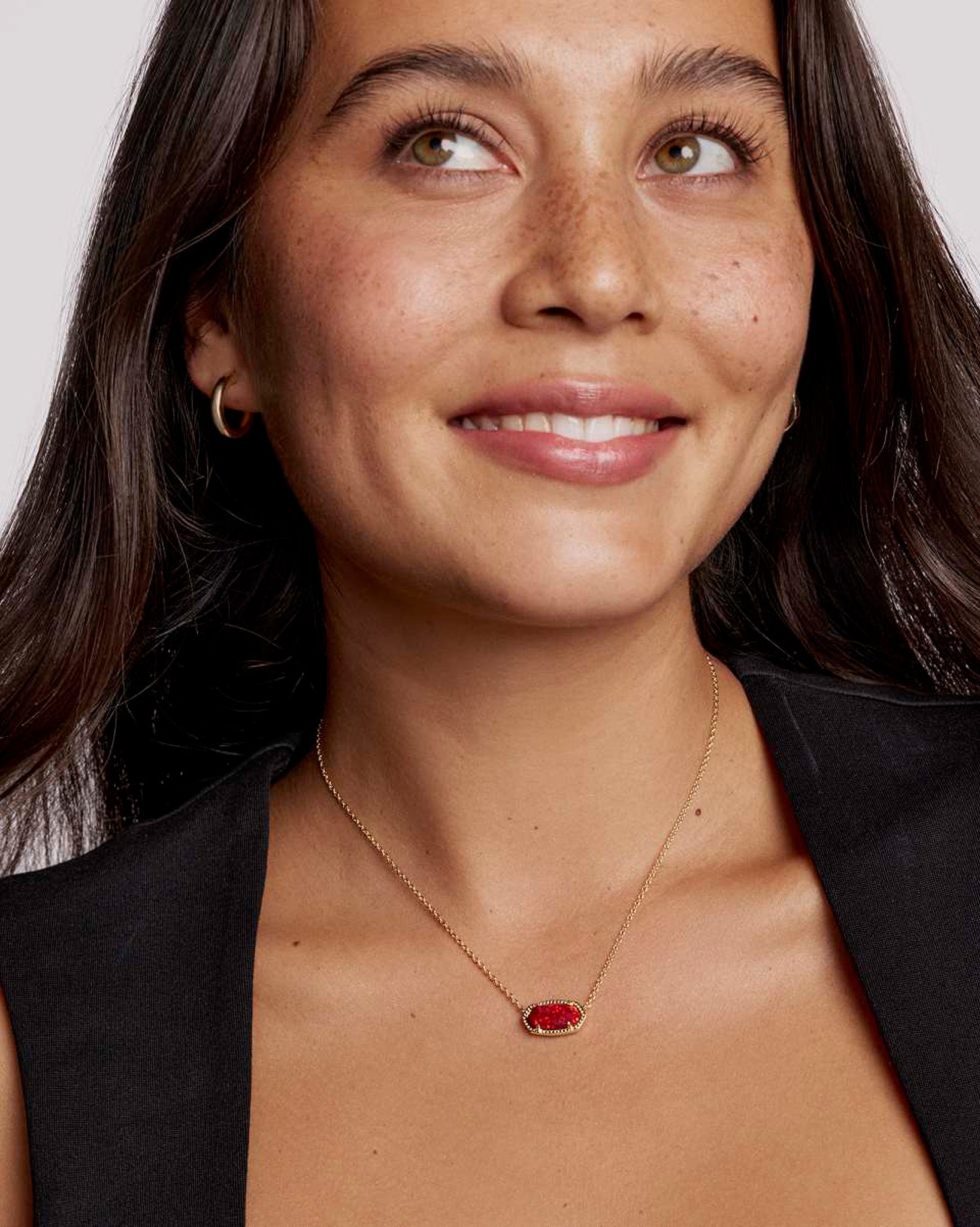 Woman wearing a necklace with an oval red pendant against a neutral background