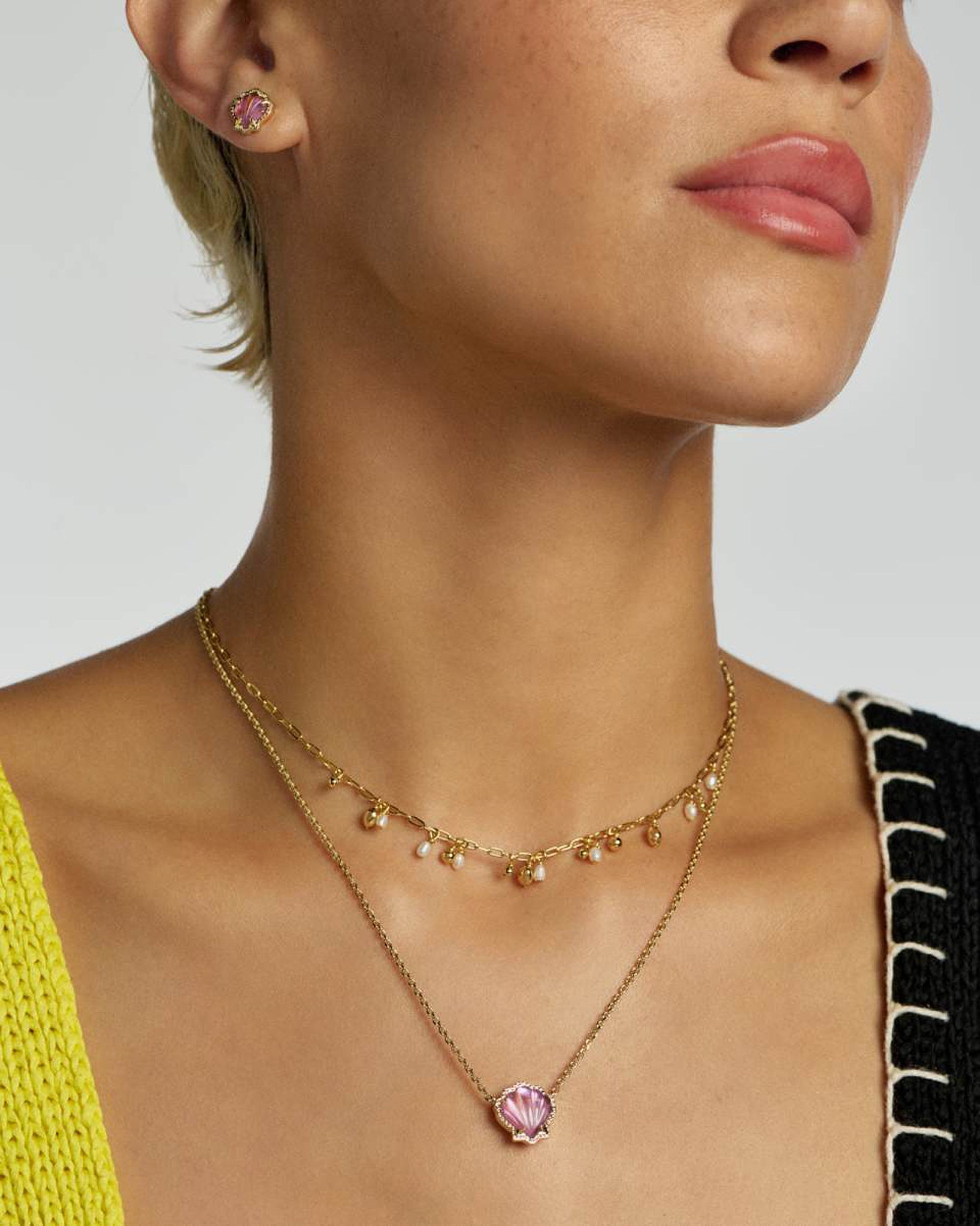 Close-up of a woman wearing a gold necklace with a pink seashell pendant on a neutral background