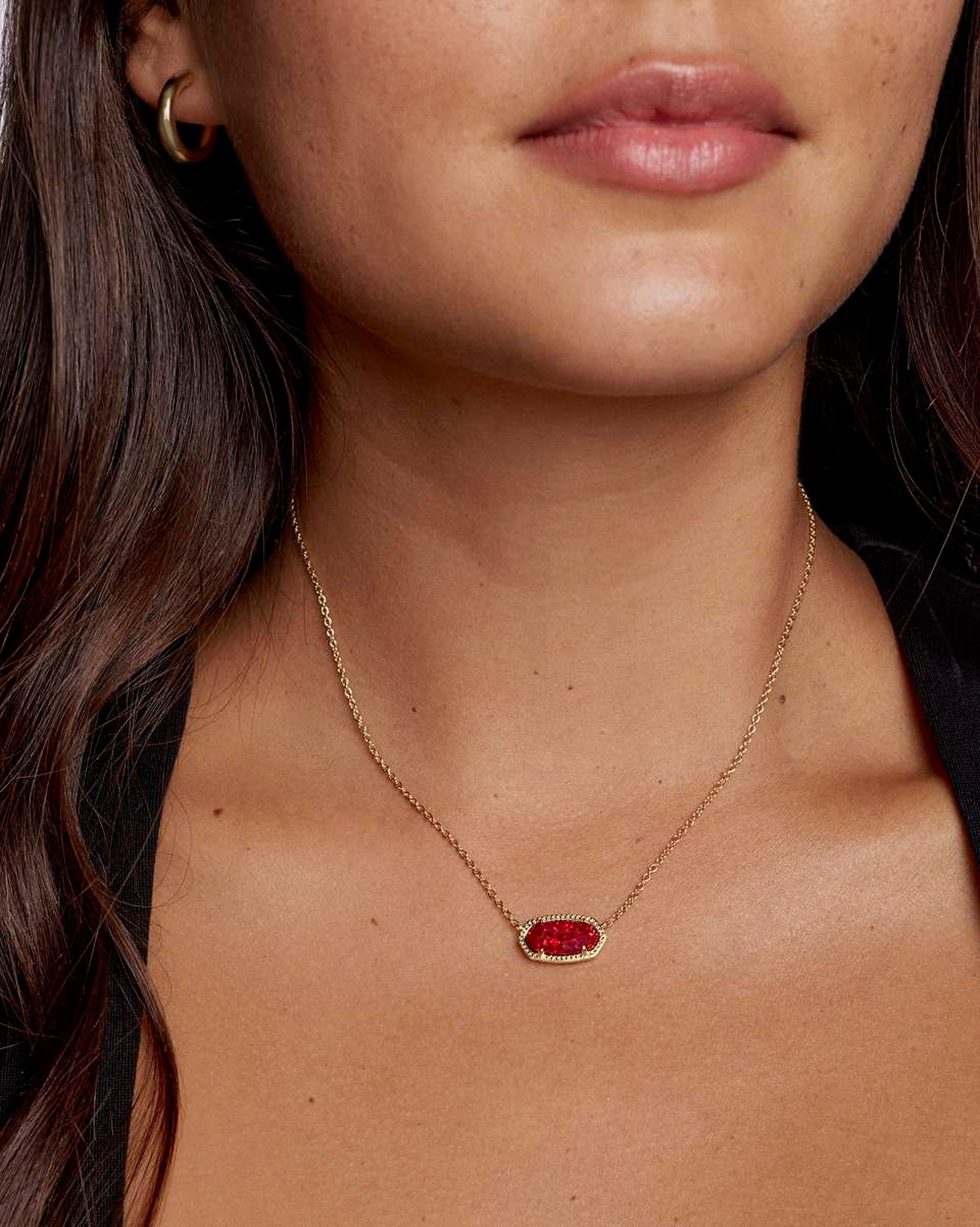 Close-up of a person wearing a gold necklace with an oval red pendant.