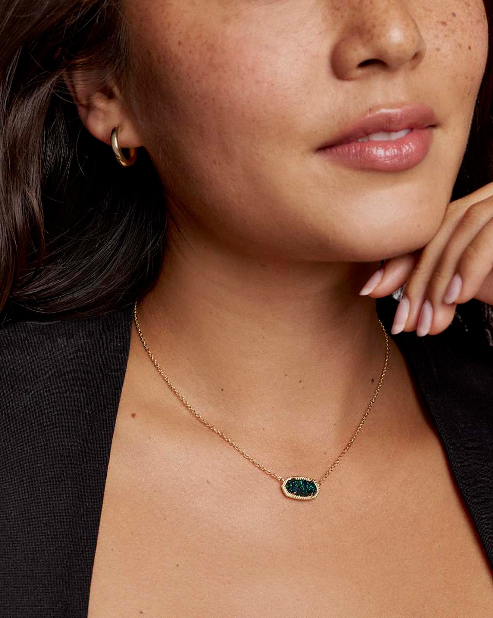 Close-up of a woman wearing a gold necklace with an oval green pendant.